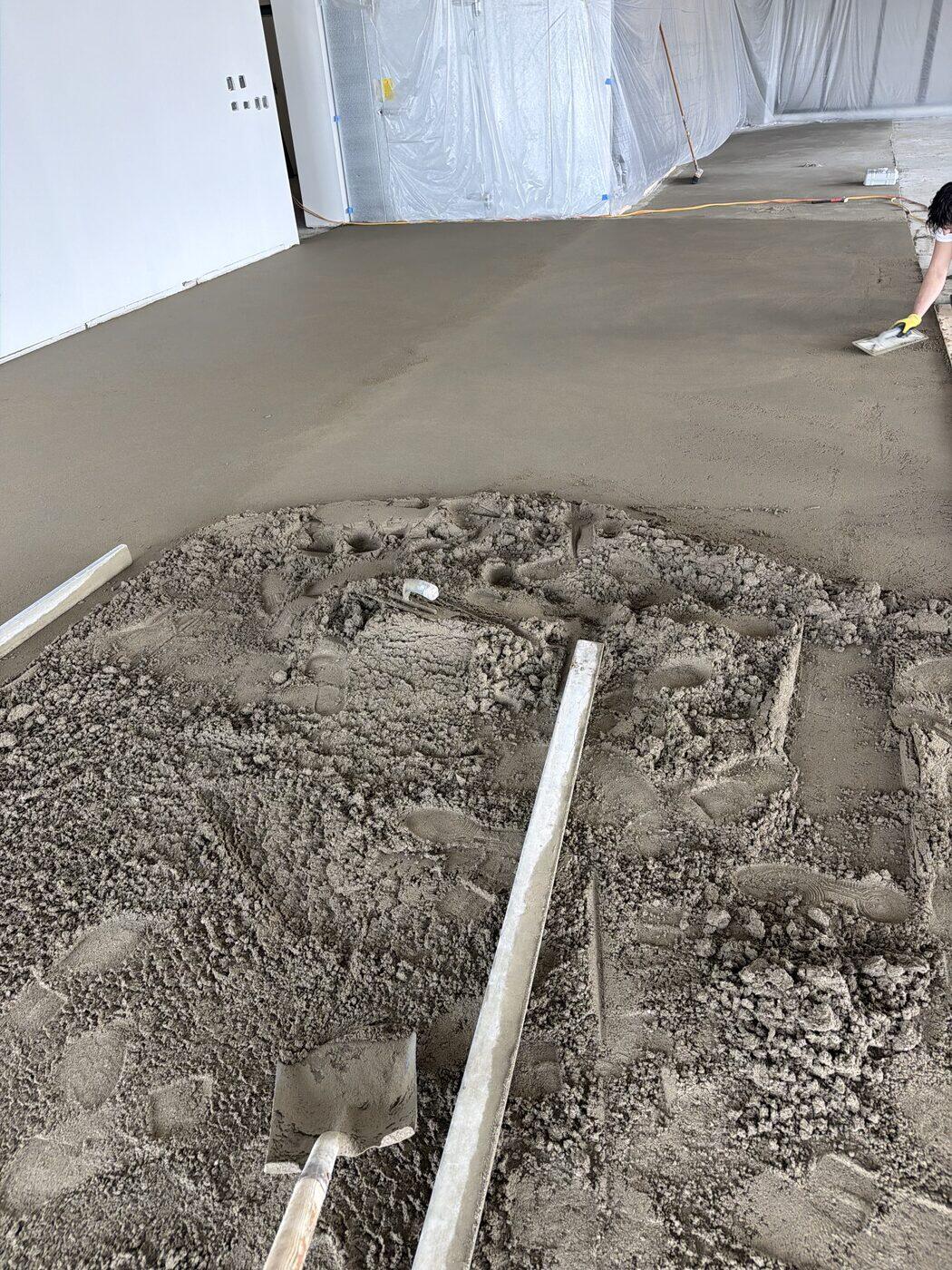 A large floor mid-pour, screed rails set across it, half the bed struck flat and half still loose mud.