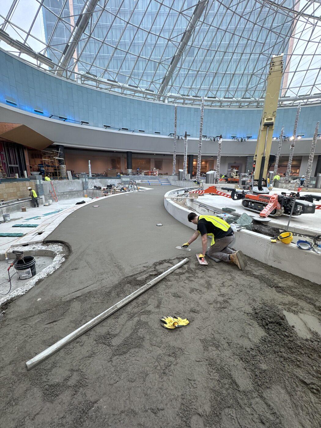 One of Cornel's sons kneeling on a mortar bed, running a hand float along its curved edge under a glass dome.